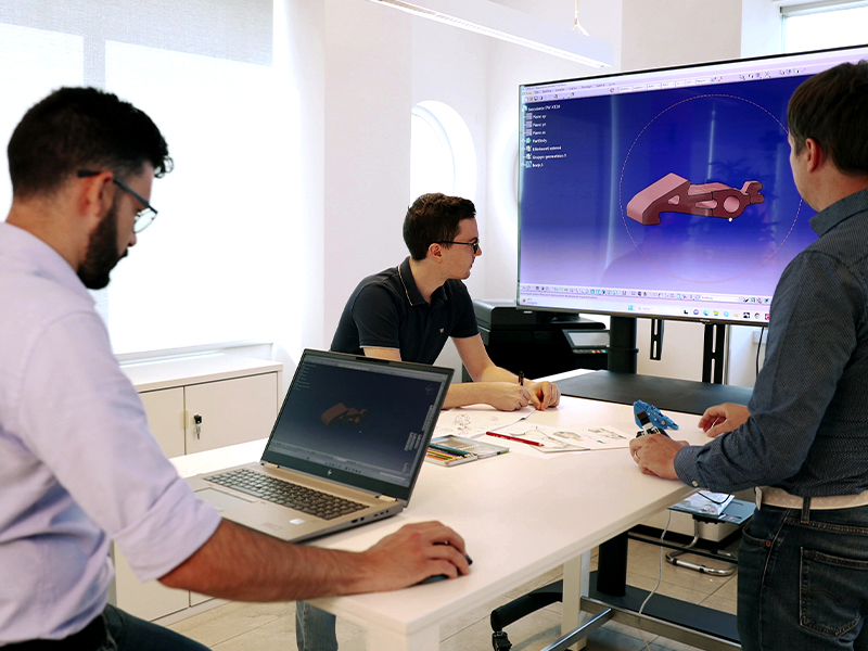 Three engineers sitting at a table during a meeting, looking at a design on a screen