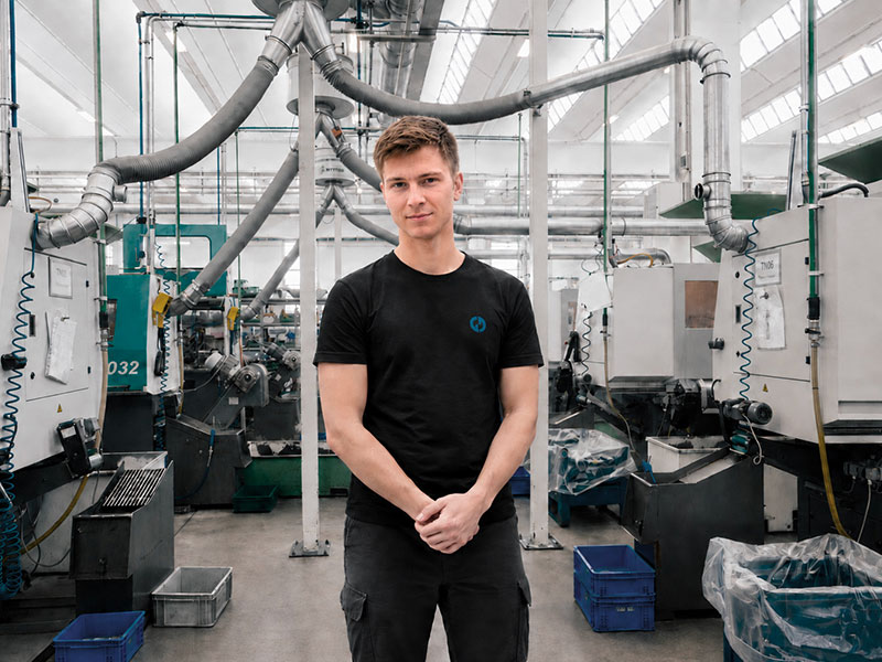 A young man posing still in front of machinery in production
